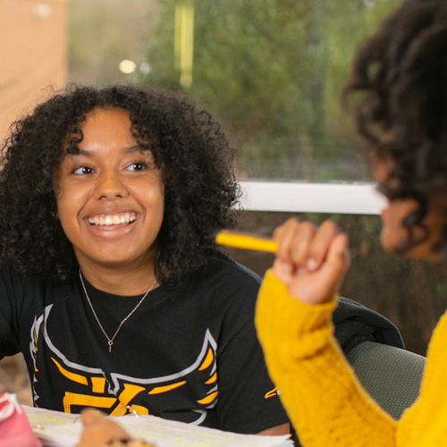 Two KSU students sit at a table, collaborating on their work 
