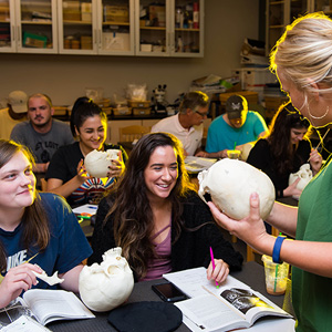 A woman teaches anatomy to a group of attentive students in a classroom setting.