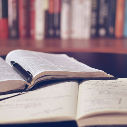An open Bible and a pen on a table, with books in the background, symbolizing self-directed learning.
