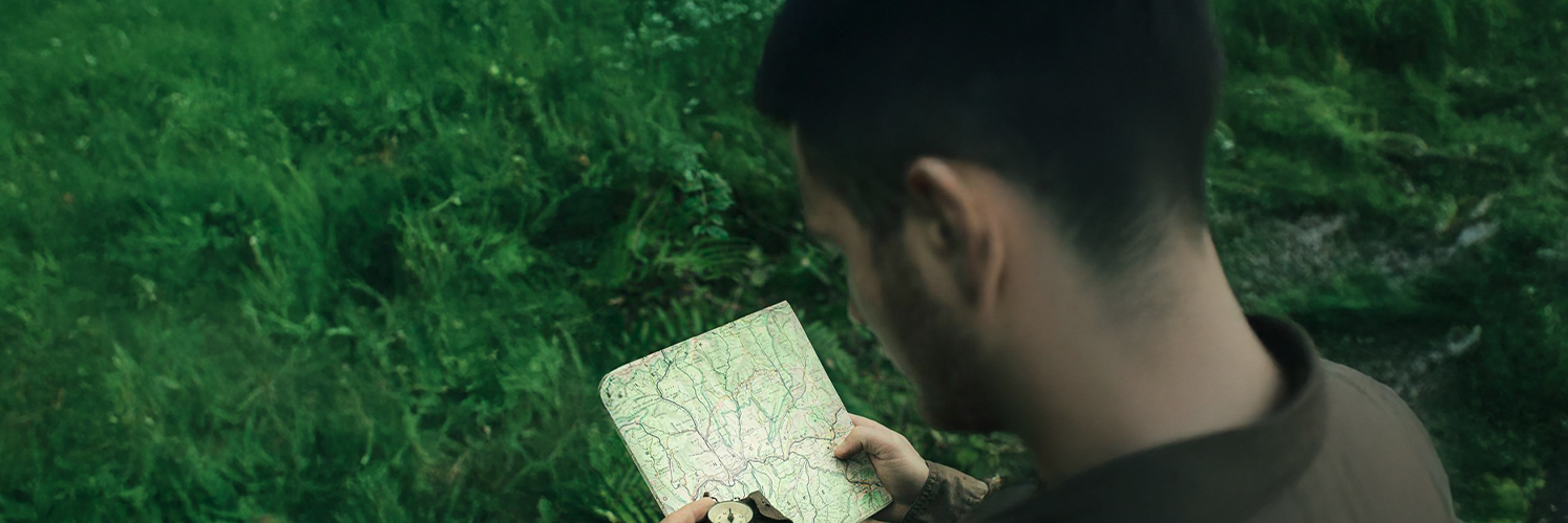 man in woods looking at compass