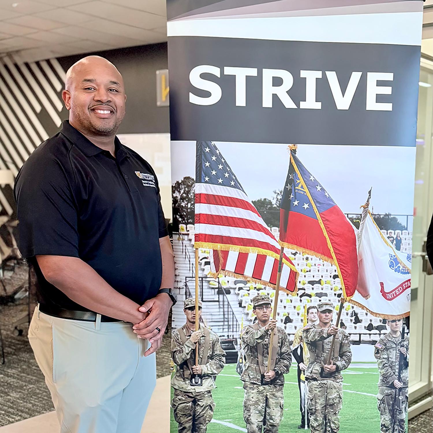 A STRIVE student stands next to a pull up banner / 