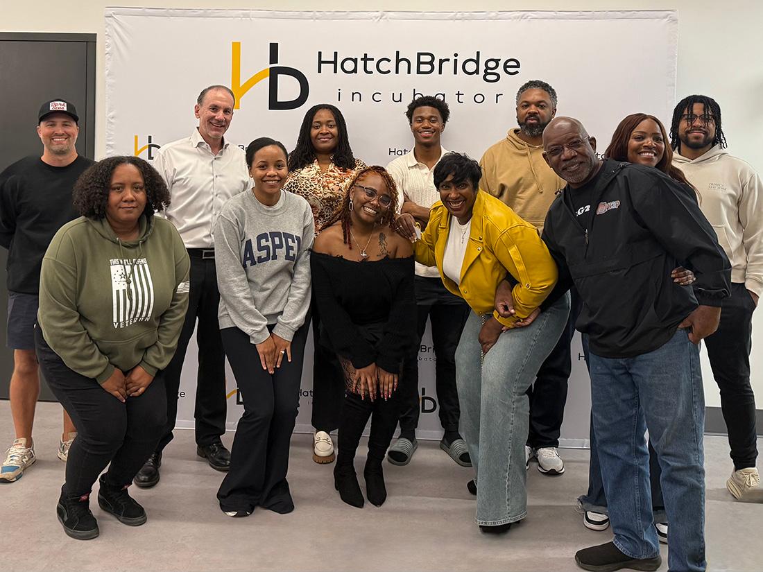 A group of STRIVE students stands together in front of the HatchBridge banner / 
