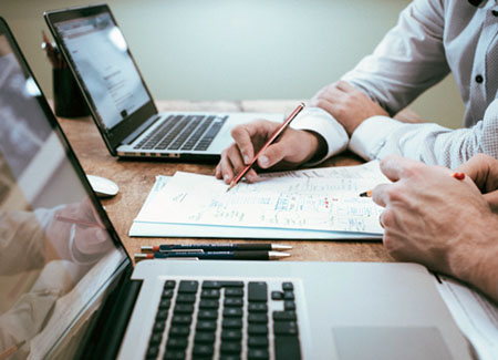 photo of someone taking notes at desk with computers