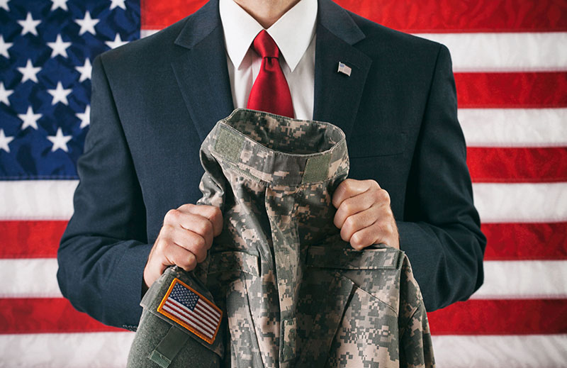 photo of man in suit in front of american flag, holding uniform