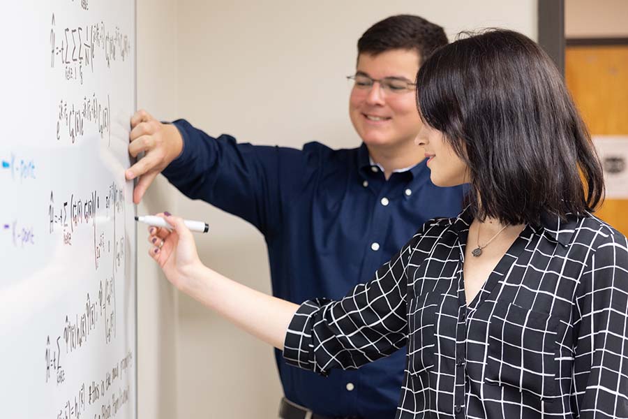 Research student working with faculty on a project / Research student writing on a white board working on formulas with another student on a research project.