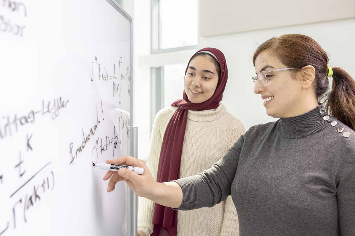 Faculty and student working on research on a whiteboard. / Faculty and student working on research on a whiteboard.