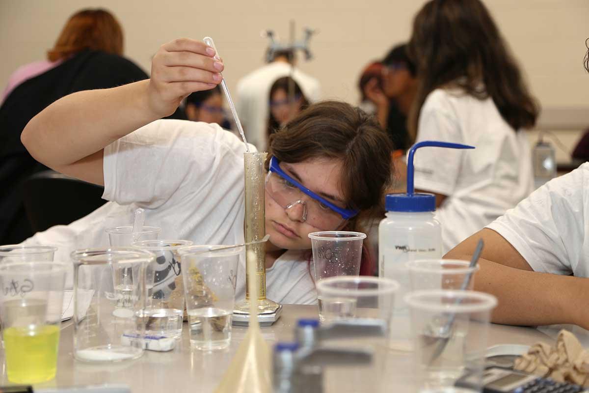 A Kennesaw State University student participating in PRESS, wears safety goggles and concentrates intently on using a dropper to add liquid to a graduated cylinder in a science course experiment in the science laboratory. / A Kennesaw State University student participating in PRESS, wears safety goggles and concentrates intently on using a dropper to add liquid to a graduated cylinder in a science course experiment in the science laboratory.