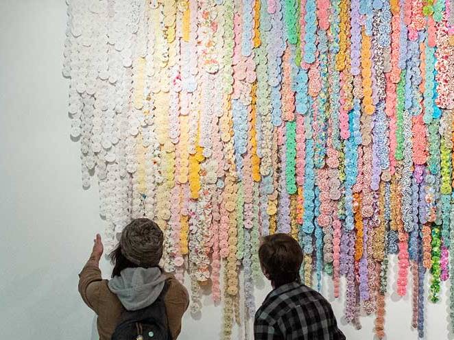 Two men are looking at a colorful art project on the wall