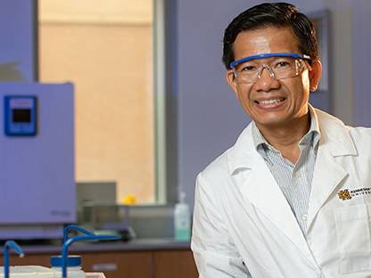 Man is wearing safety goggles and lab coat smiling for a picture