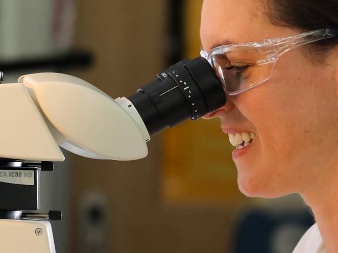 Woman wearing safety goggles and looking through a biology microscope