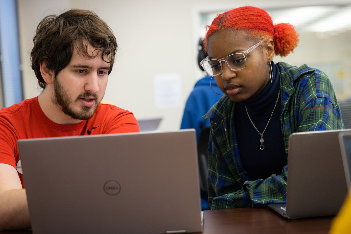 Two students both focusing on a laptop having a conversation