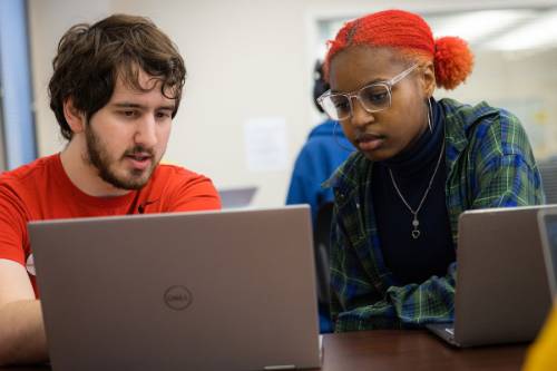 Two students looking at laptop communicating with eachother