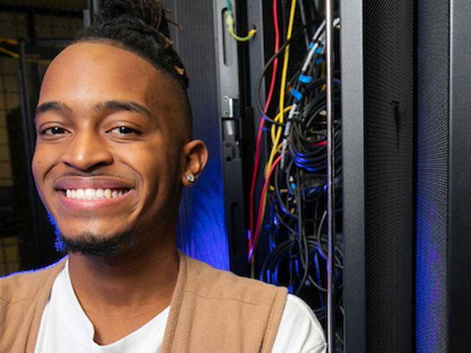 Man smiling for picture standing infront of a eletric panel with wires coming out of it