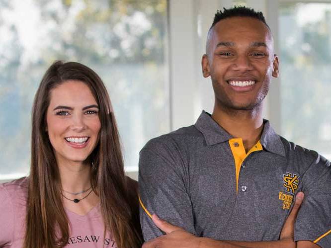 two ksu students standing in front of a window smiling for picture