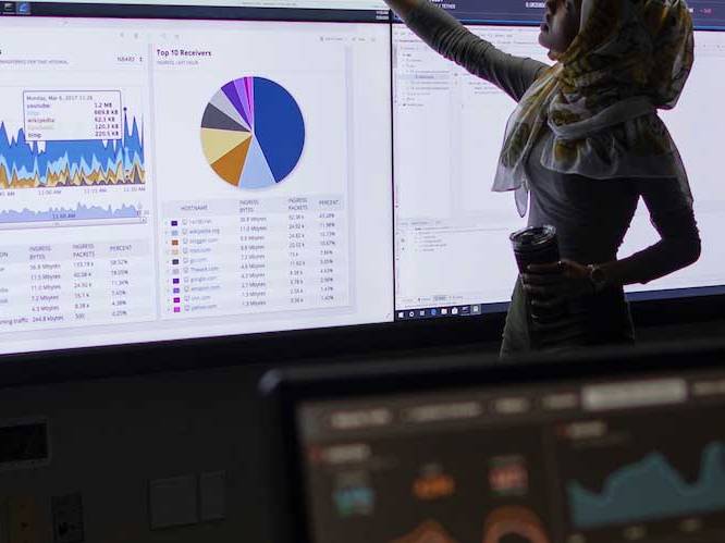 Woman standing infront of projector screen pointing to graphs on screen