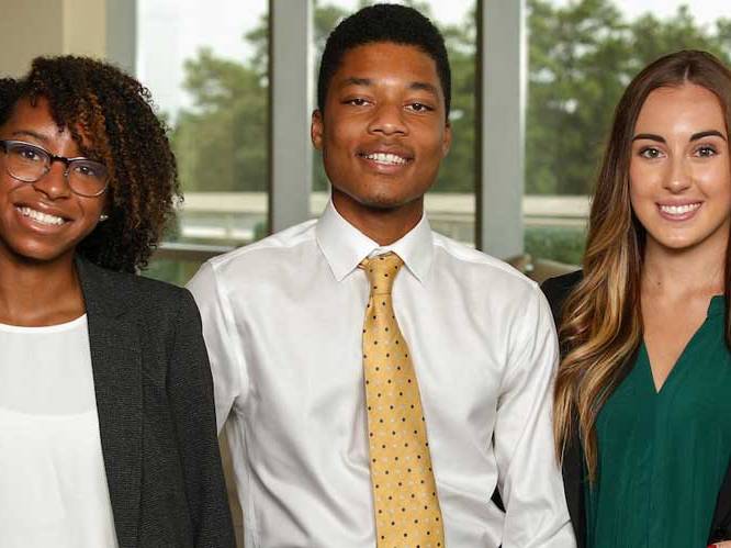 Three business students standing together smiling for a picture