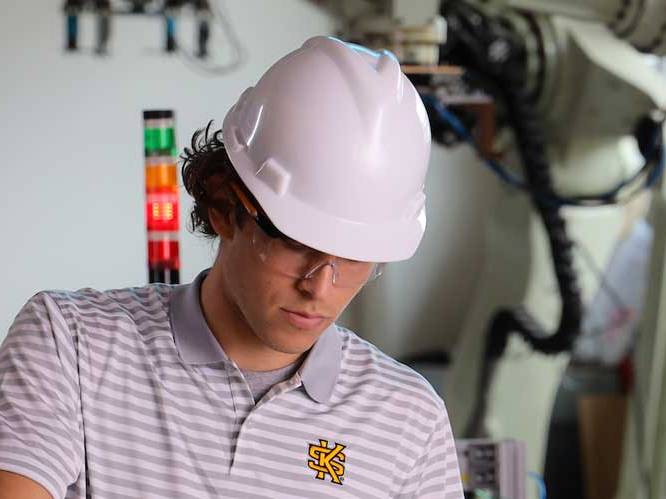 Student wearing safety goggles and hard hat focusing on project