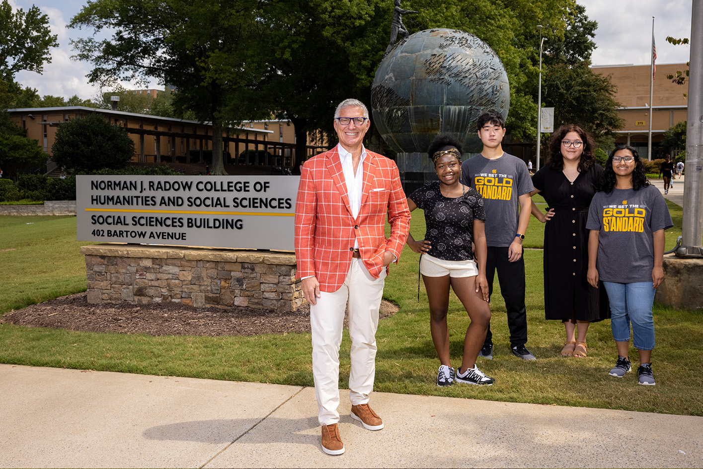 group of students huddled around the building sign exterior of KSU's Radow