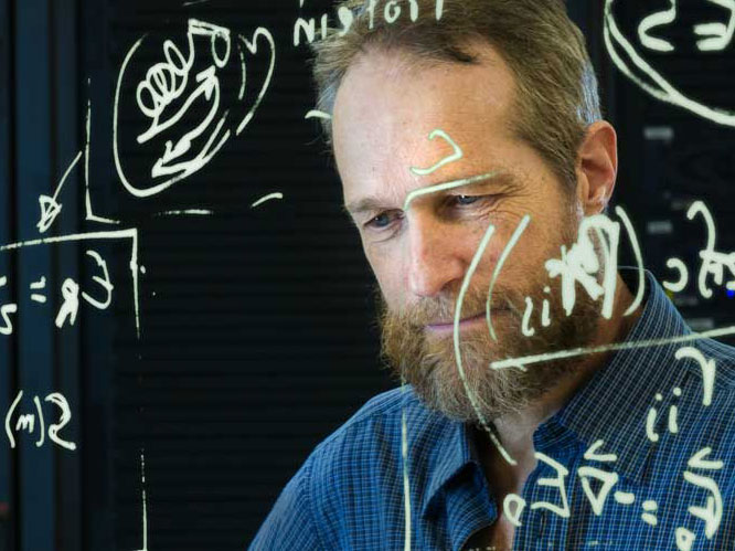 Man looking at a large piece of glass with math equations on it