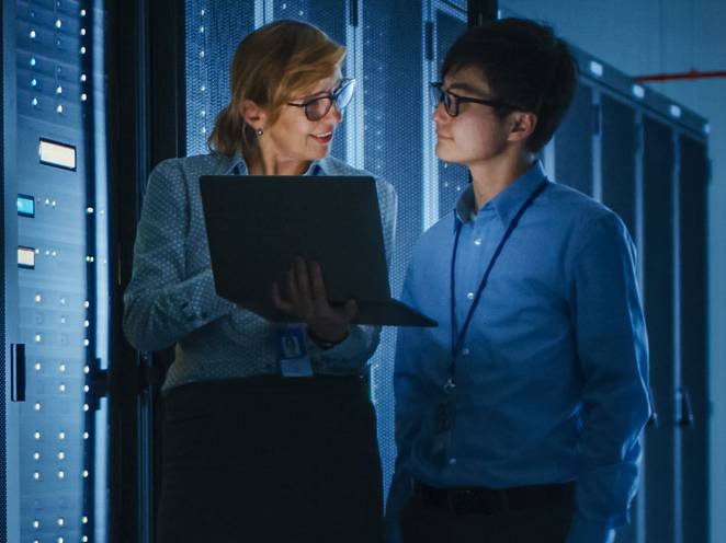 Man and woman standing holding a laptop communicating