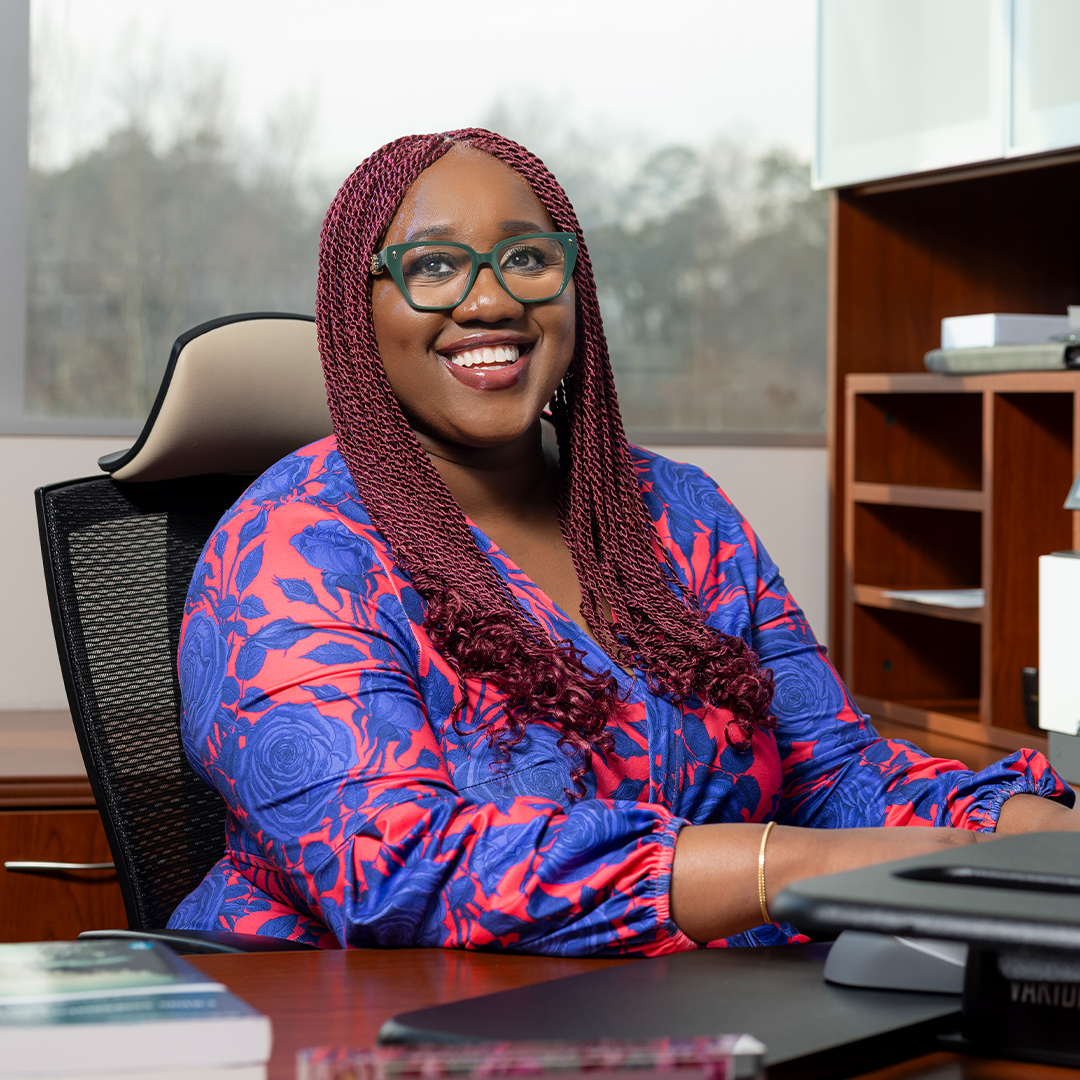 female faculty member in floral print shirt smiling at her desk while typing