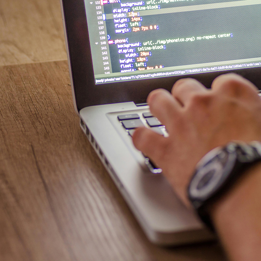 close up on mans hands as he types on computer with coding on screen