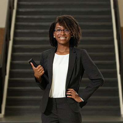  student in business attire front of stairs holding laptop