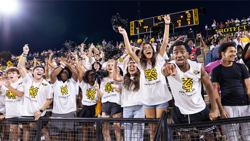 KSU Football fans in white KS tshirts cheering at a KSU football game