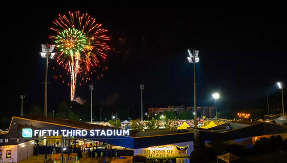 Colorful fireworks illuminate the night sky above Kennesaw State stadium during a large event at sunset.