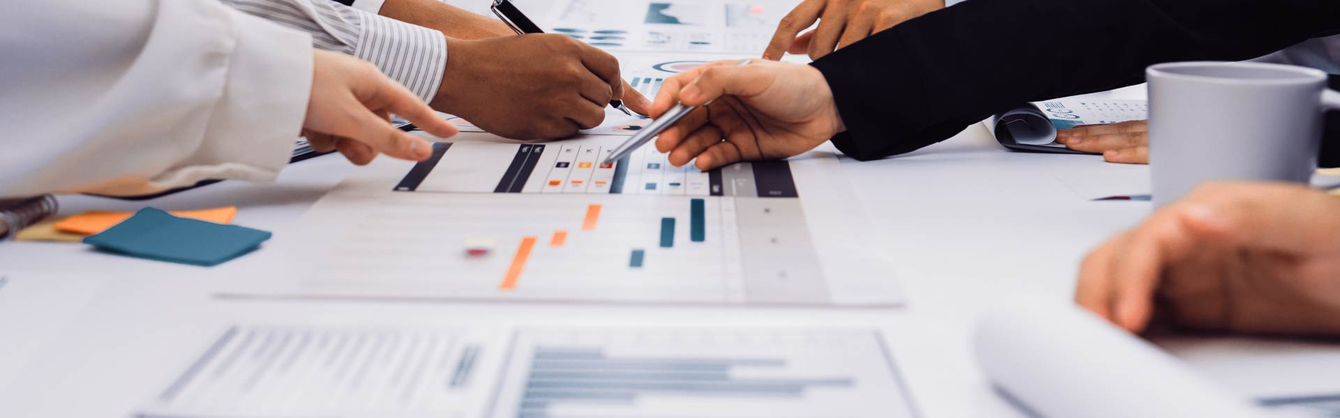 businessmen and businesswomen pointing at a variety of charts and graphs scattered on a table