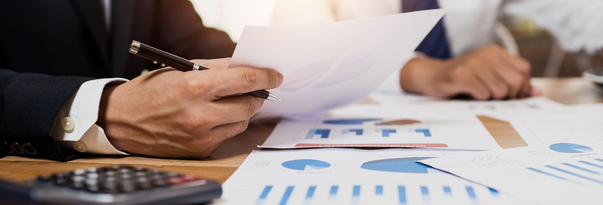 Business man holding a document and pen, with financial charts and graphs on a table