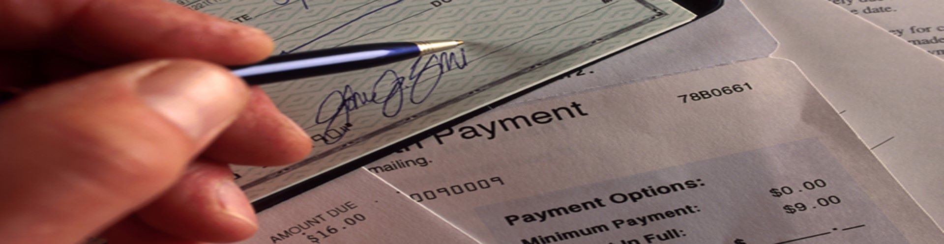 A hand holding a pen and signing a check