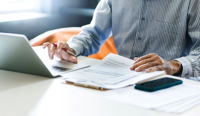 Businessman using laptop and reviewing documents on a clipboard