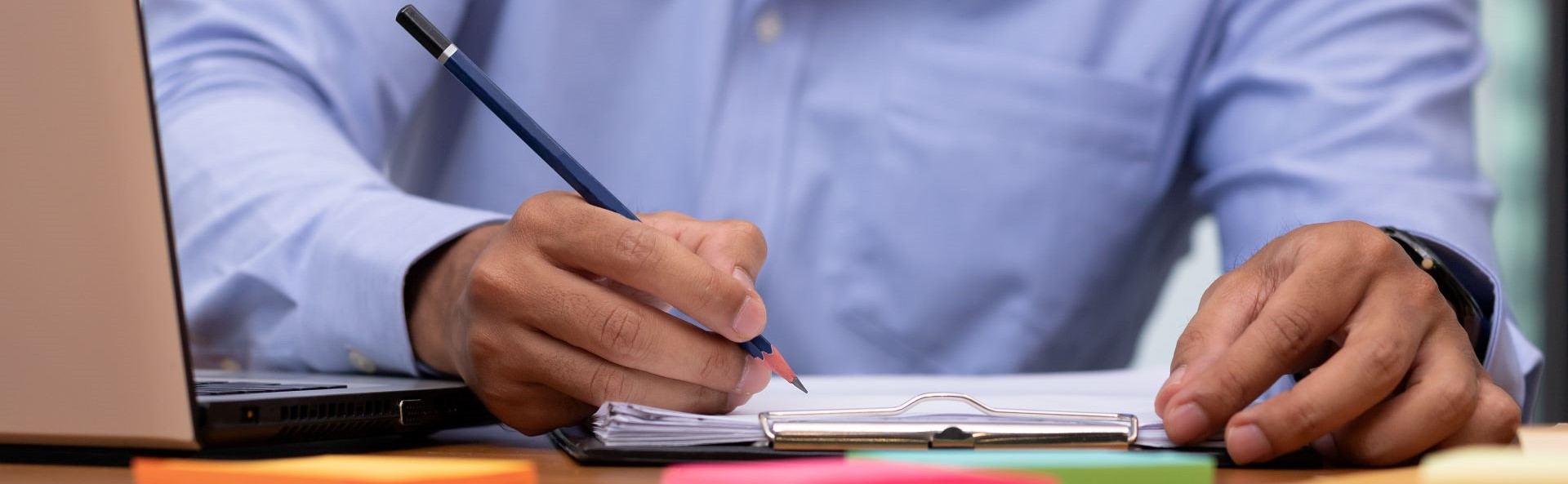 Man holding a pencil and writing a note on a clipboard