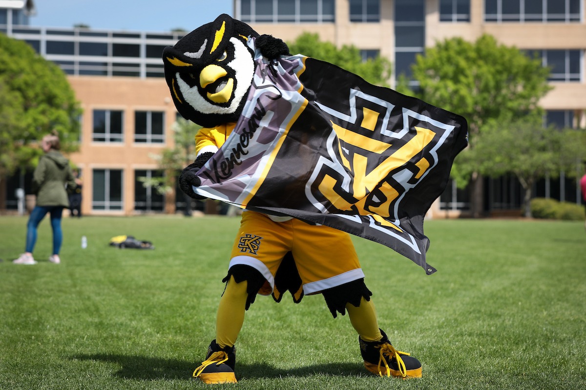 mascot scrappy on campus green holding waivng ksu flag
