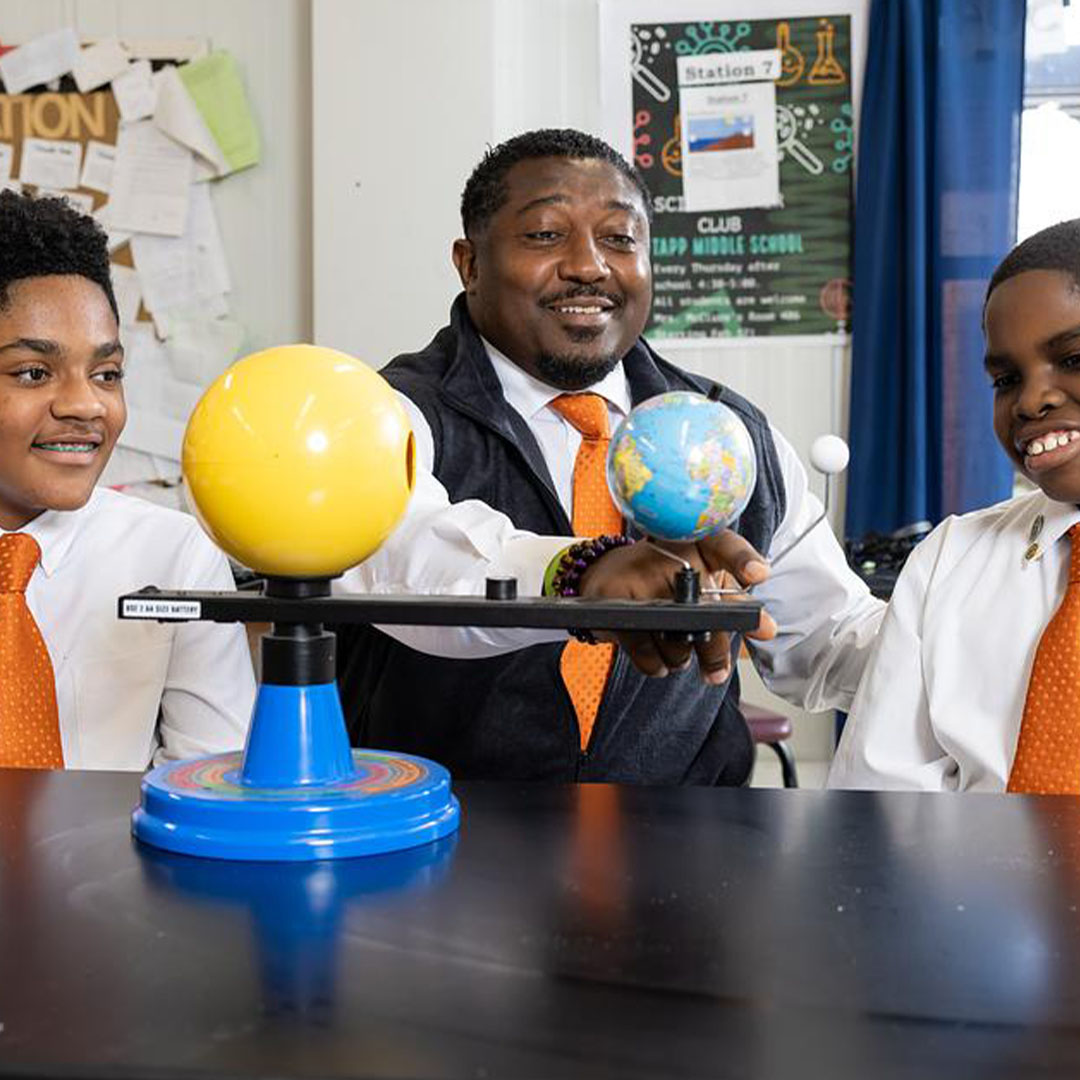 Educator demonstrating a classroom science activity with students using a model and globe