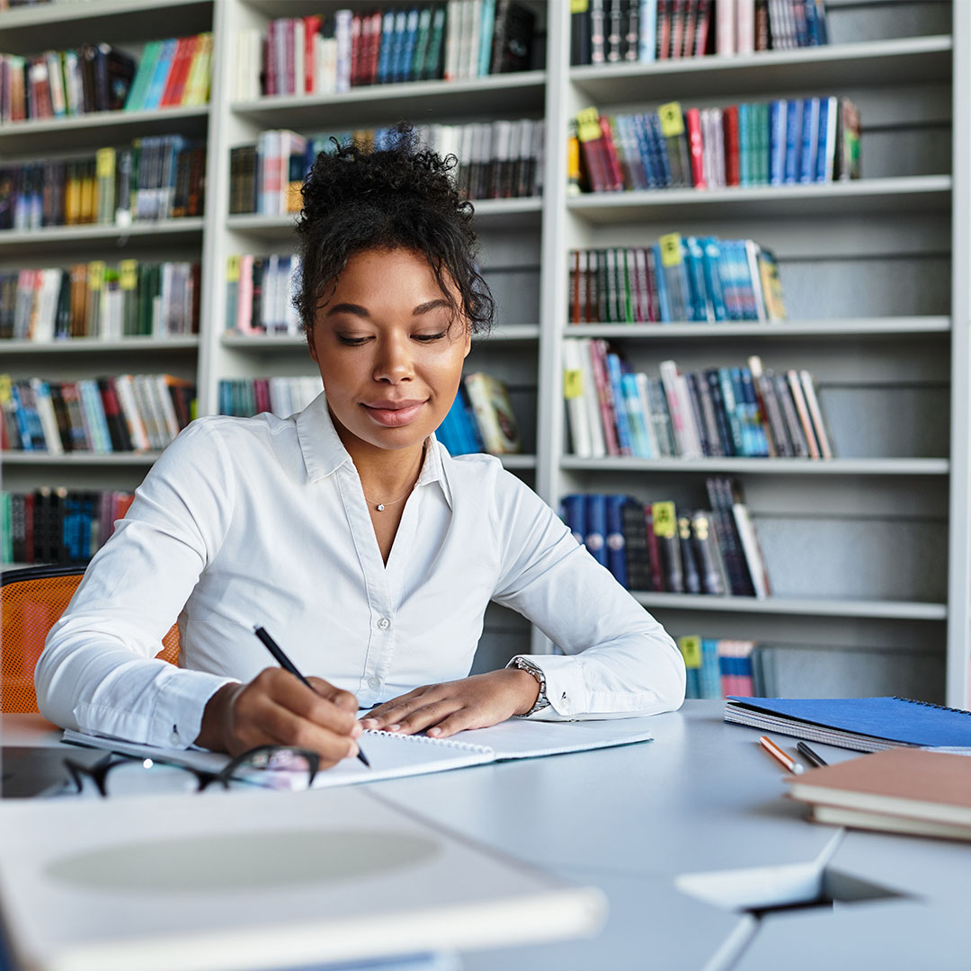 A female smiling at desk as she write on paper
