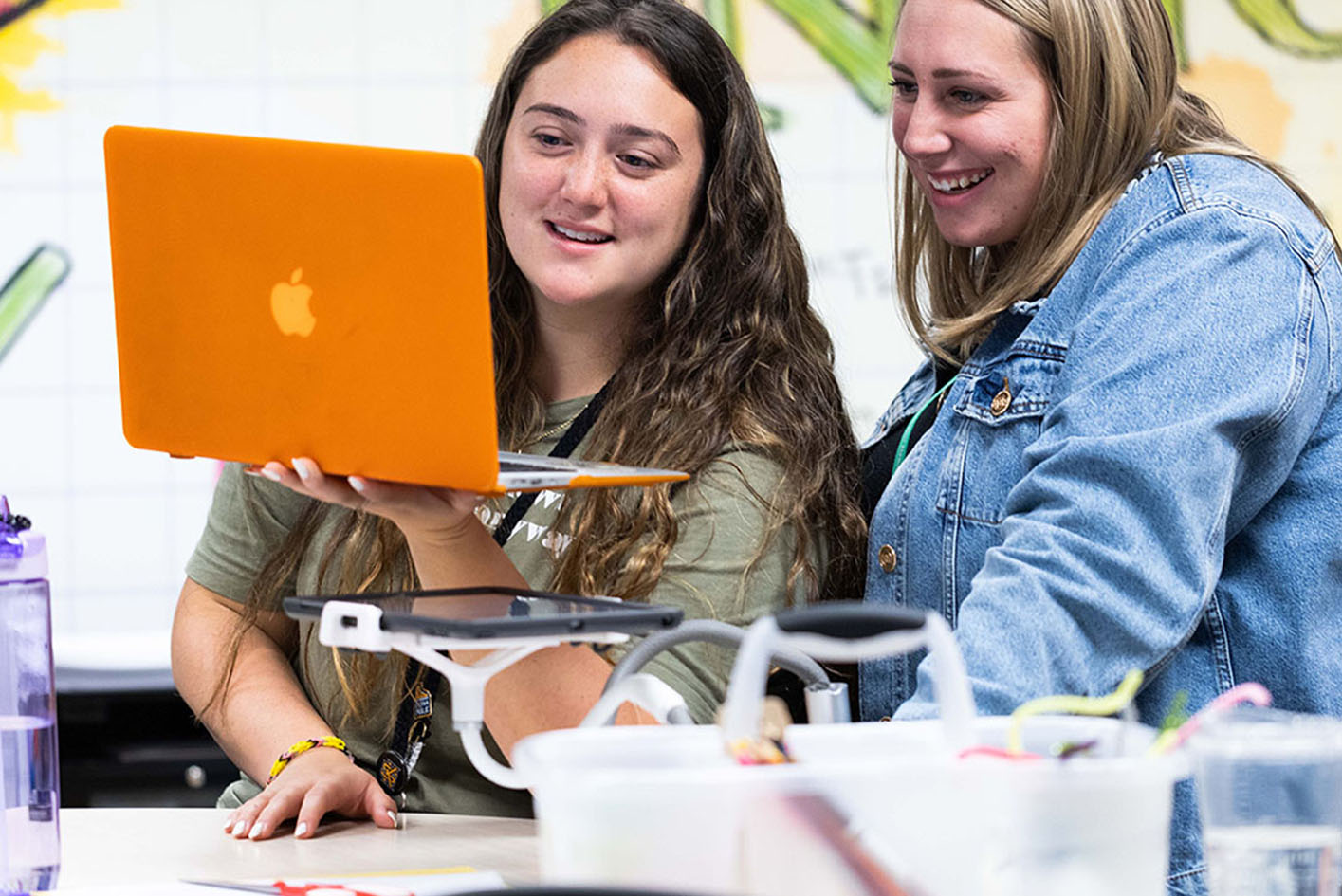 Two graduate students review coursework together while looking at a laptop in a collaborative classroom setting.