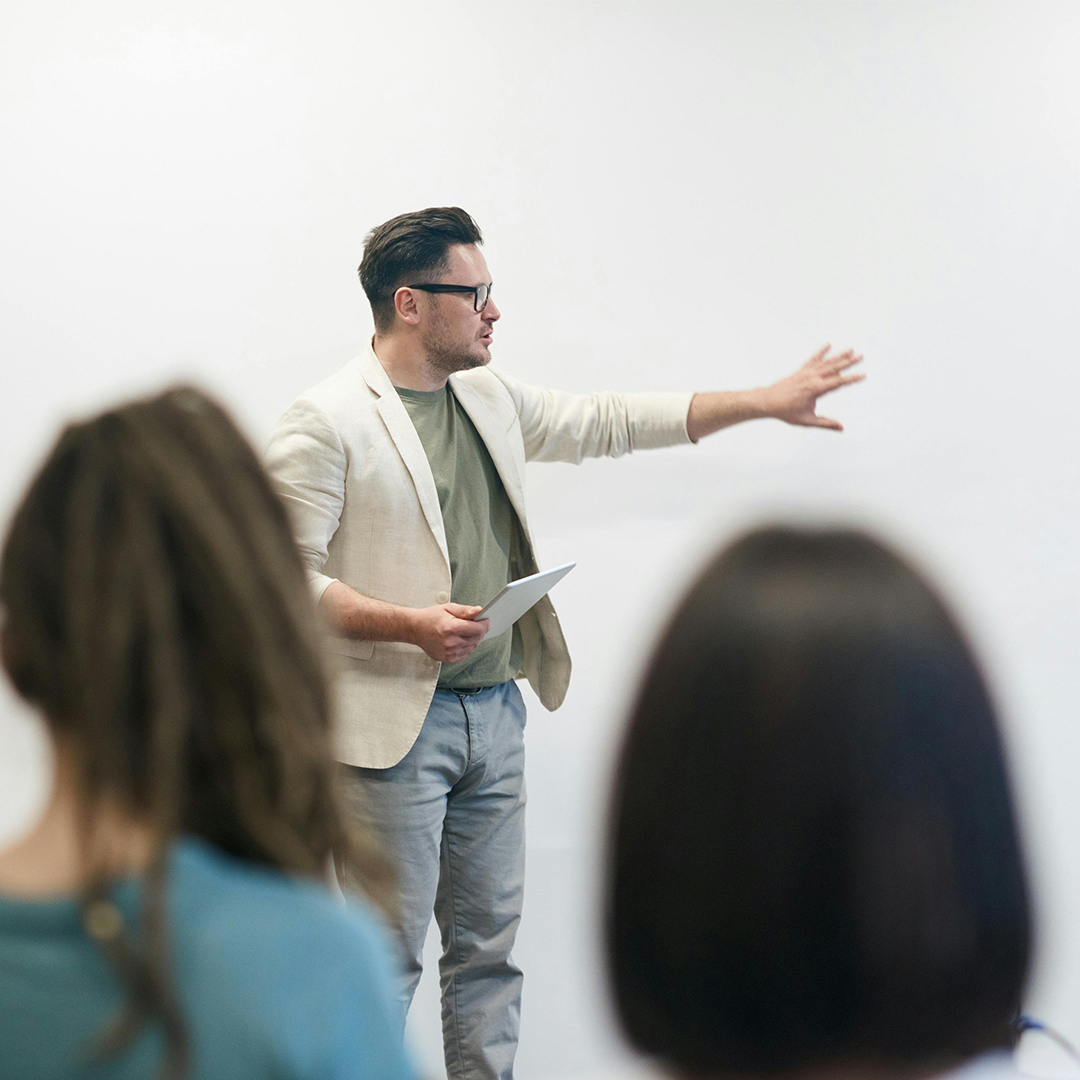 A man in a suit pointing to board as he gives presentation