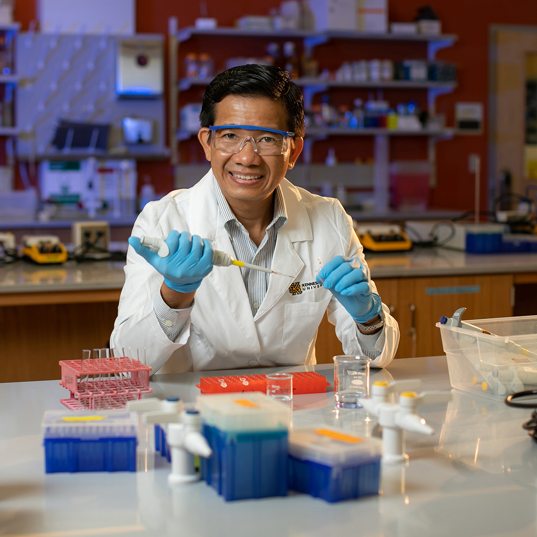 A smiling male scientist in a lab coat and gloves is holding a pipette, engaged in laboratory experimentation.