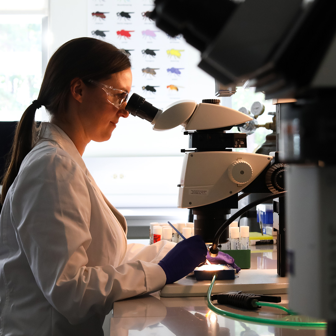A female scientist in a lab coat examines samples in a laboratory filled with various scientific instruments.