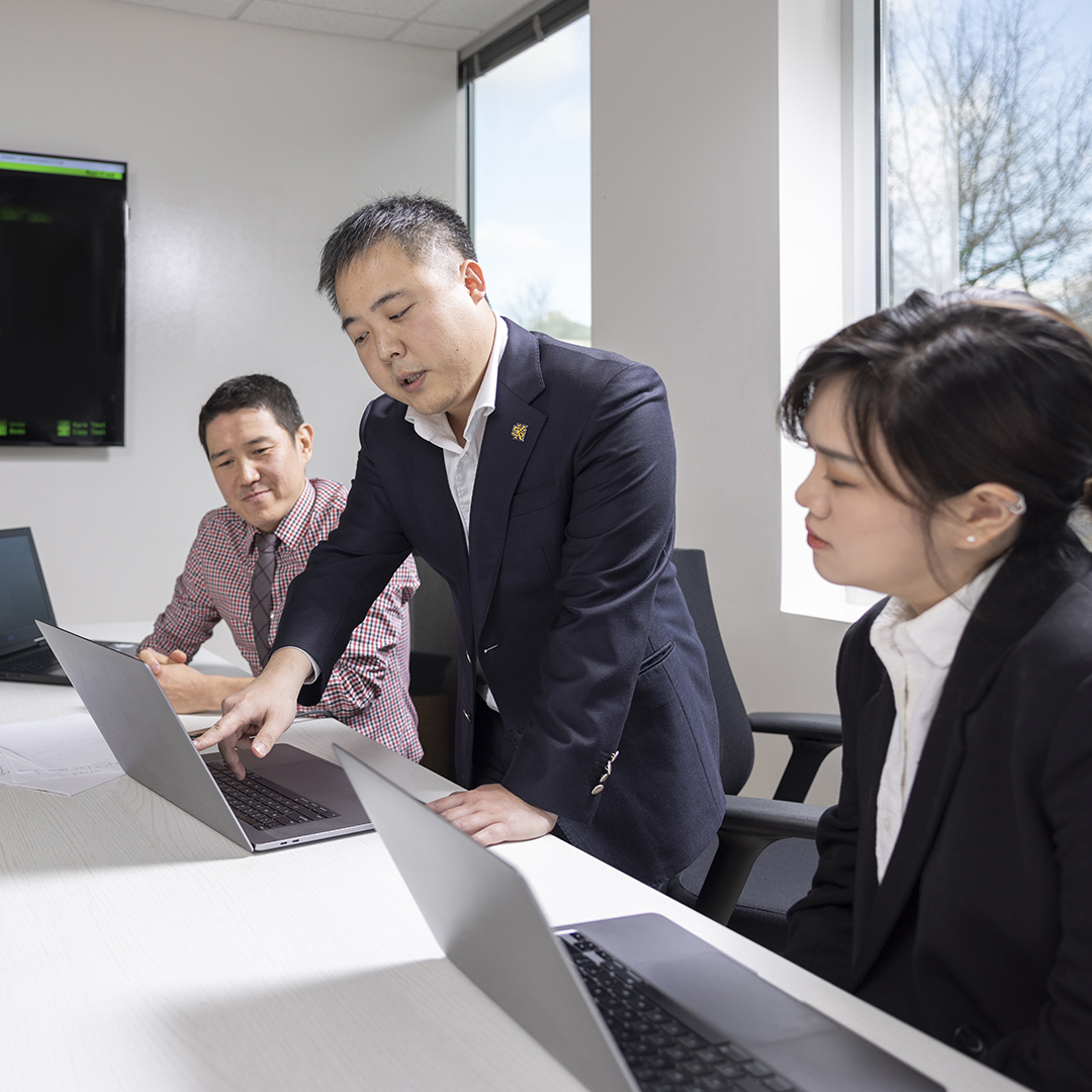 Group working on laptops in a modern office with a server tower and large screen displaying code.