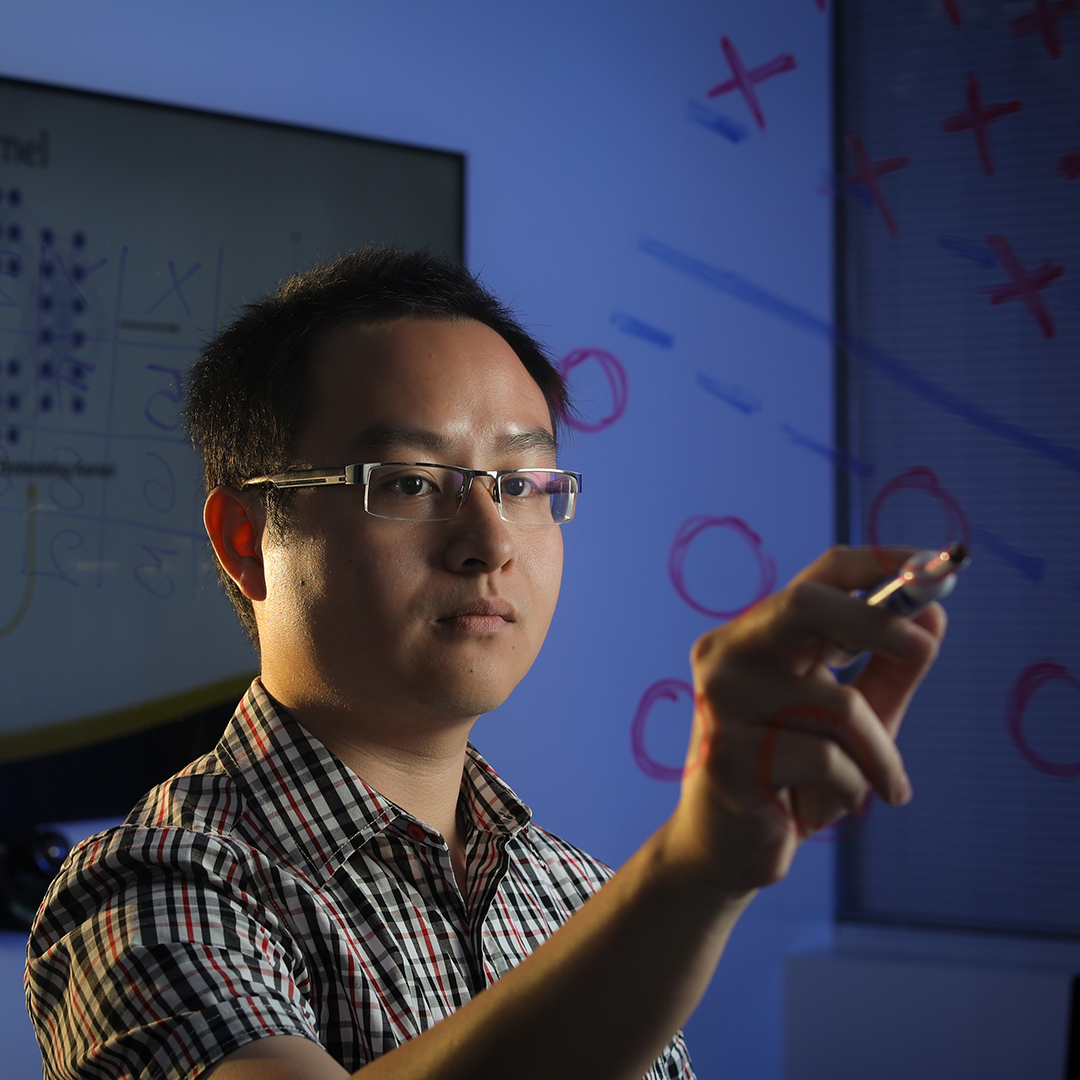 Man writing mathematical and algorithmic diagrams on a transparent board.