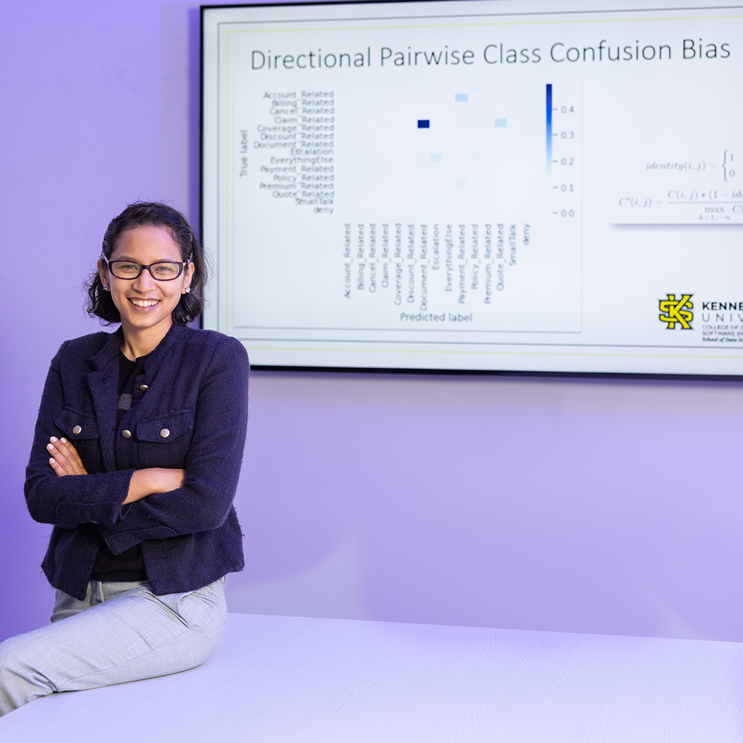 Woman sitting on a table in front of a screen displaying a presentation with data charts.