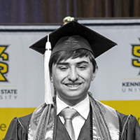 Male student smiles at KSU commencement in cap and gown