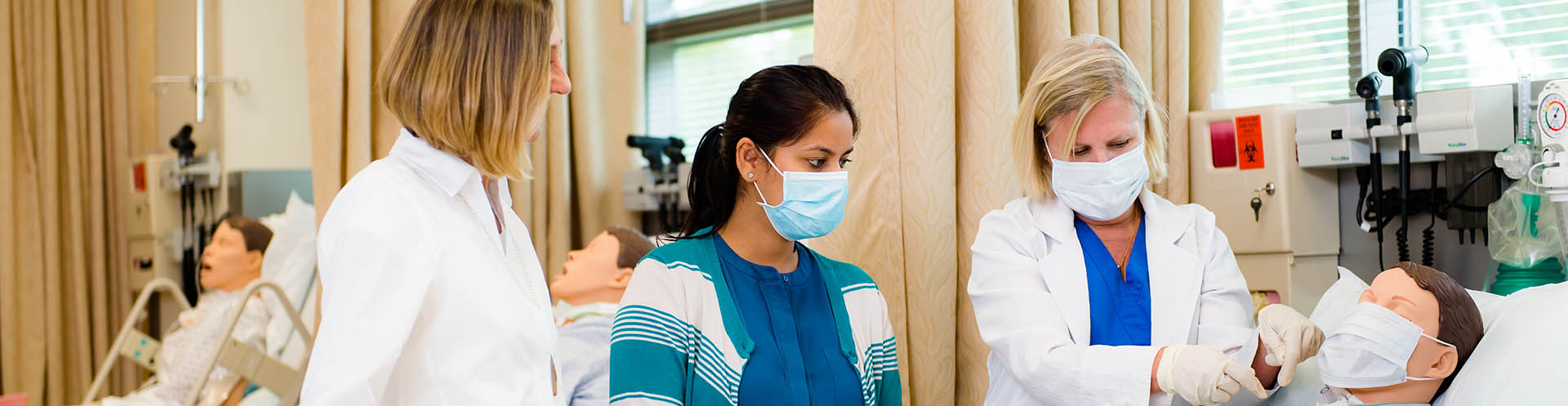 An instructor shows how to perform a procedure on a practice dummy in a working classroom setting.
