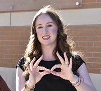 Female student showing KSU spirit hand sign, Hooty Hoo.