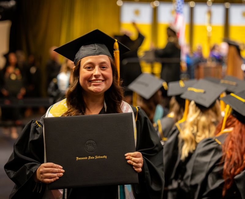 A graduate in cap and gown holds a diploma at a commencement ceremony