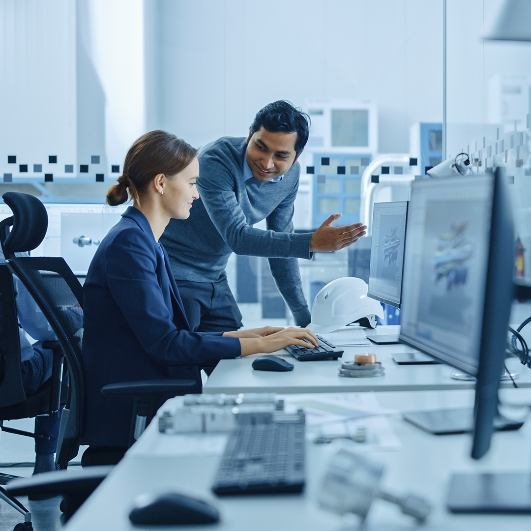 Two people focused on their computers while collaborating in a modern office setting.