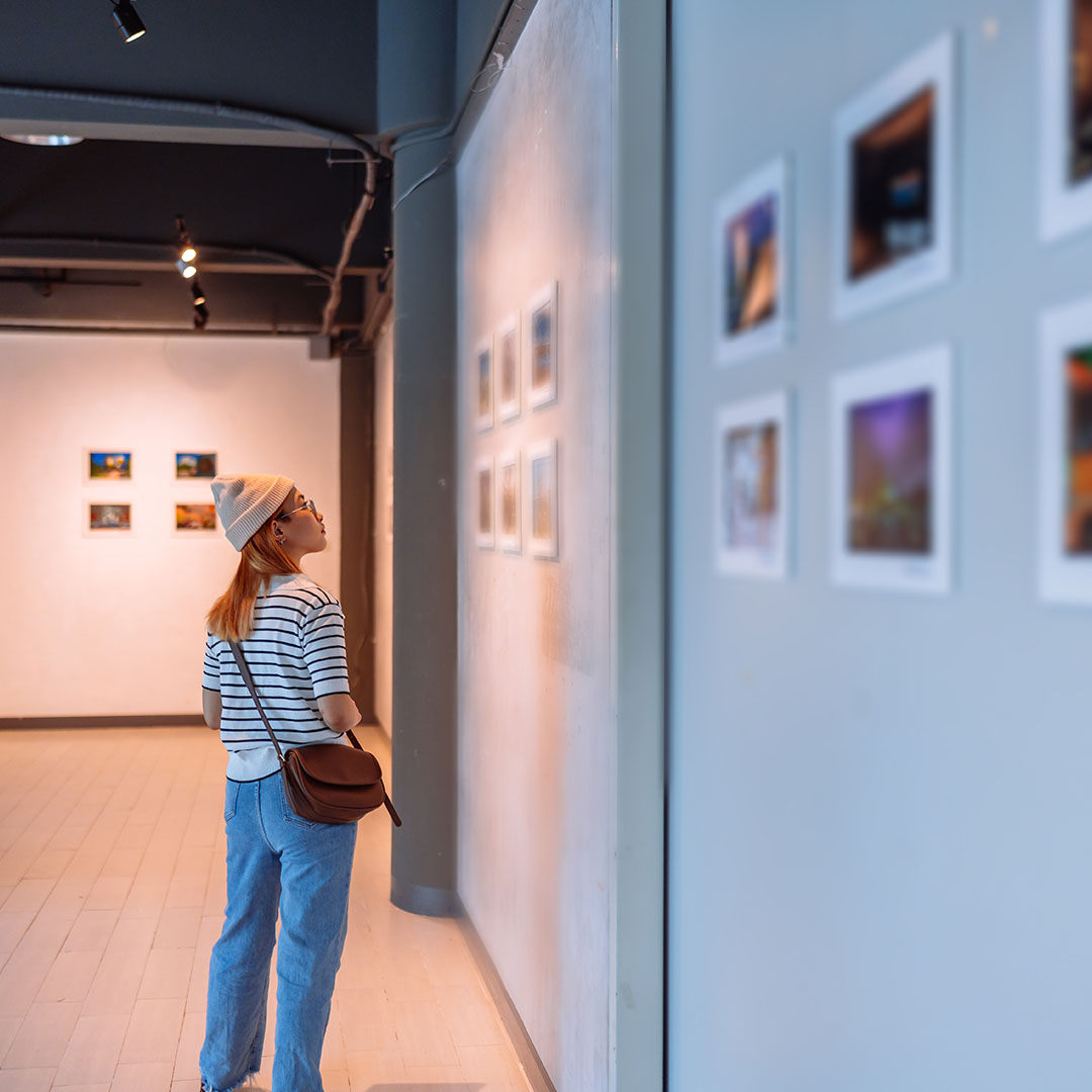 A visitor standing in a modern art gallery, observing framed artwork displayed along the walls.